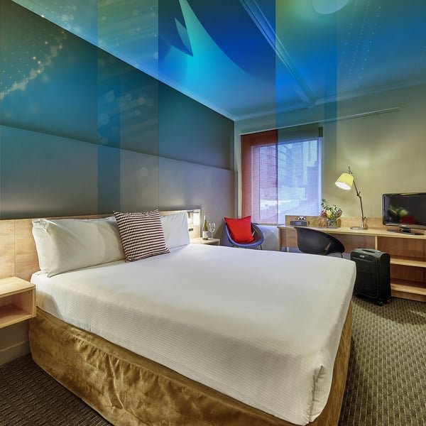 A hotel room with a double bed, a red armchair and a desk by the window