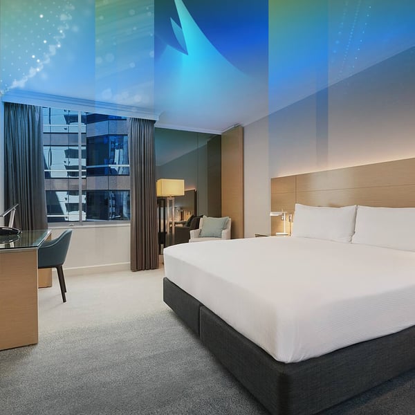A hotel room with a king bed, a desk and a city view through the window