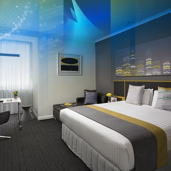A hotel room with a king bed, a sofa and city skyline artwork